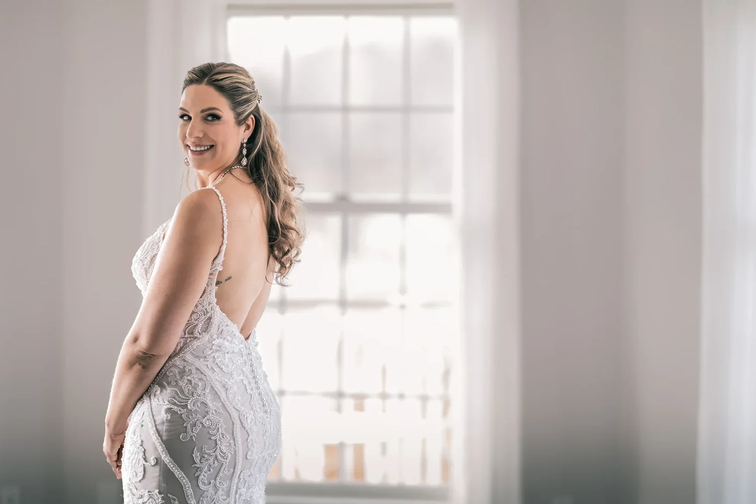Charissa in her lace gown looking back over her shoulder by a tall window in the Manor House