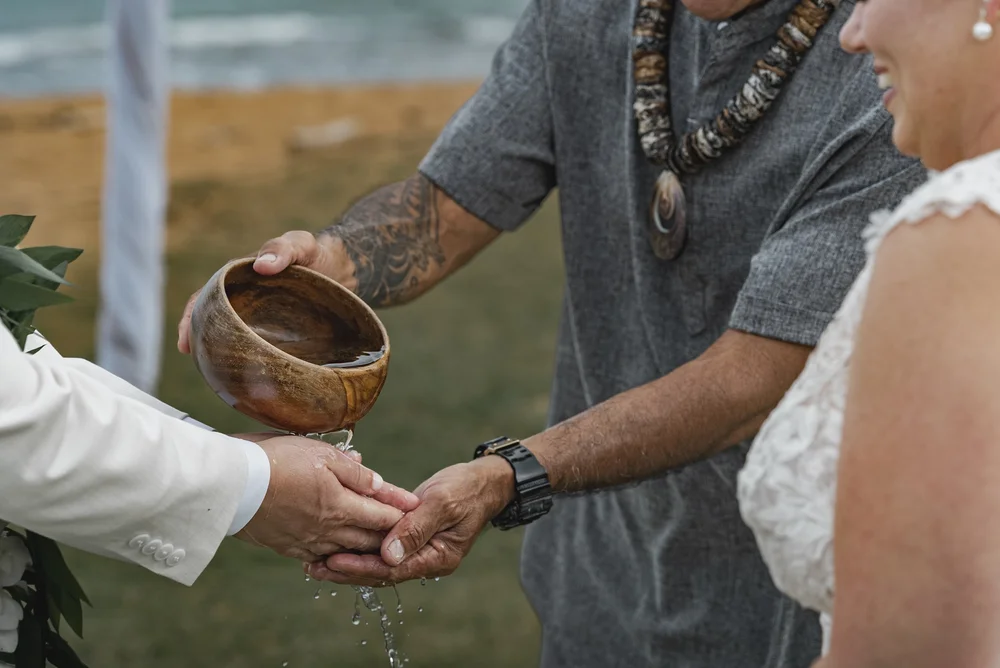Water poured from a wooden bowl over joined hands during an outdoor wedding ceremony.