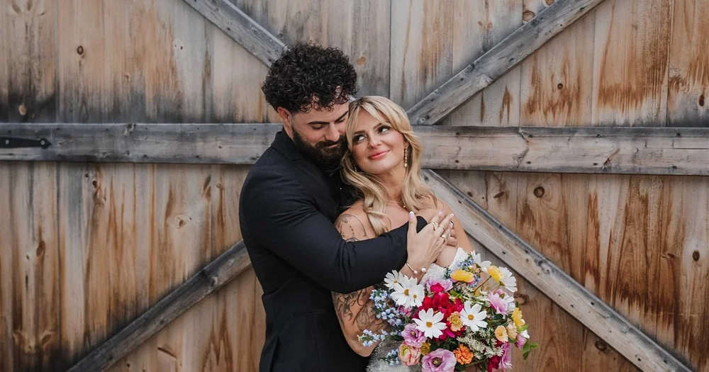 A couple embracing in front of weathered barn doors at The Stone Barn at Beardslee Farm in Little Falls, New York