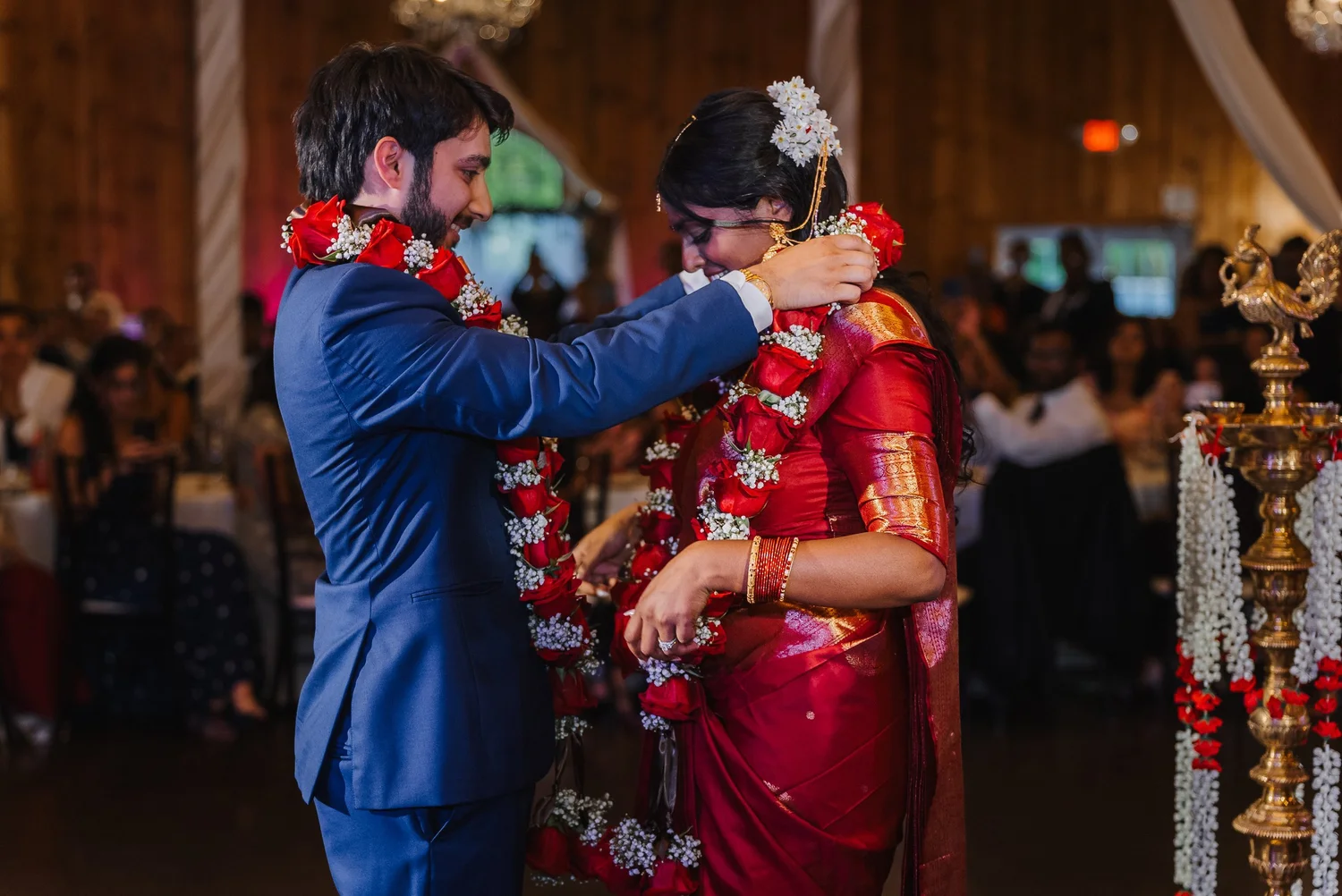 Ansel and Natalia exchanging red and white flower garlands in the barn, Natalia wearing red