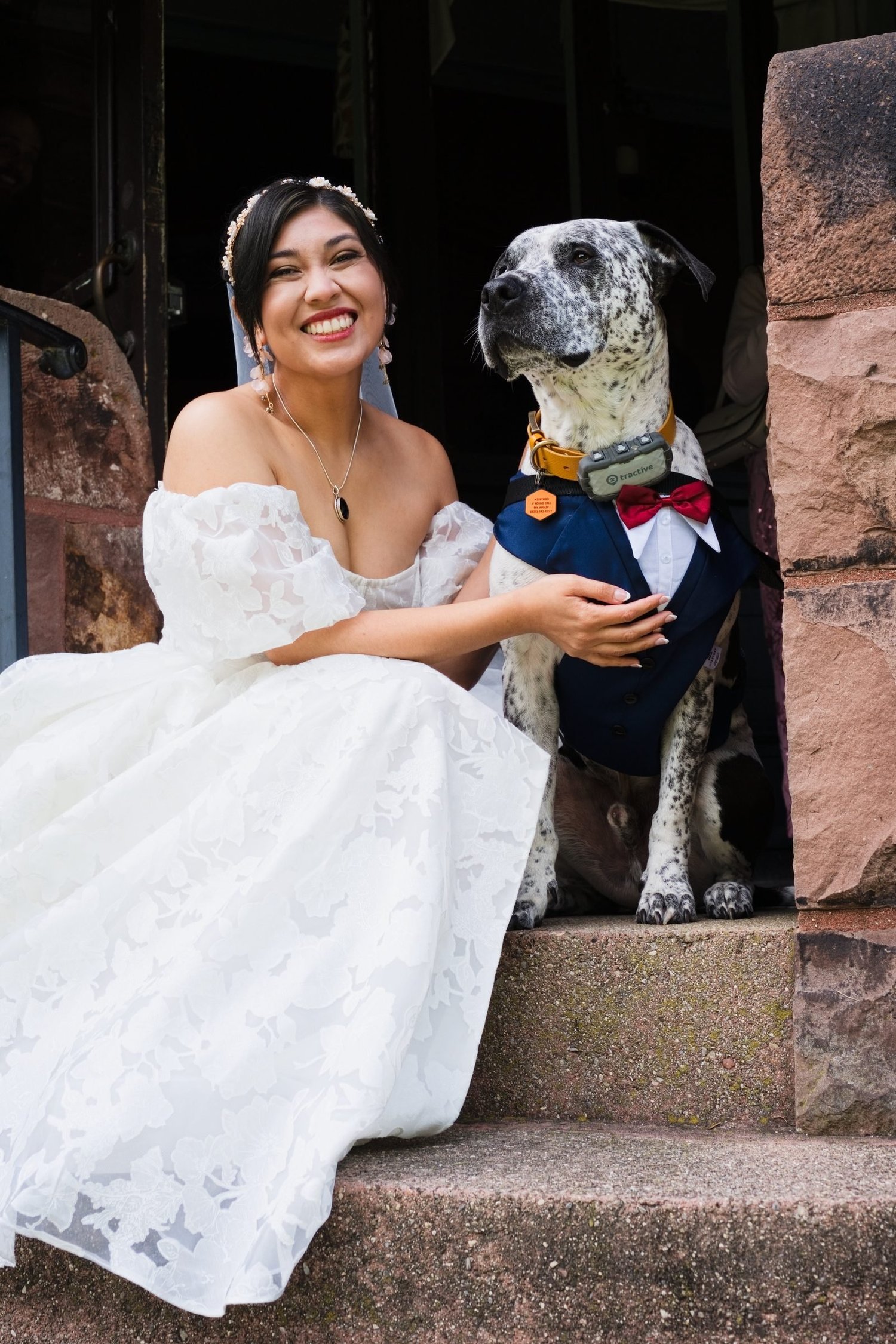 Marseille sitting on red stone steps next to her spotted dog, who is dressed in a navy jacket and red bow tie