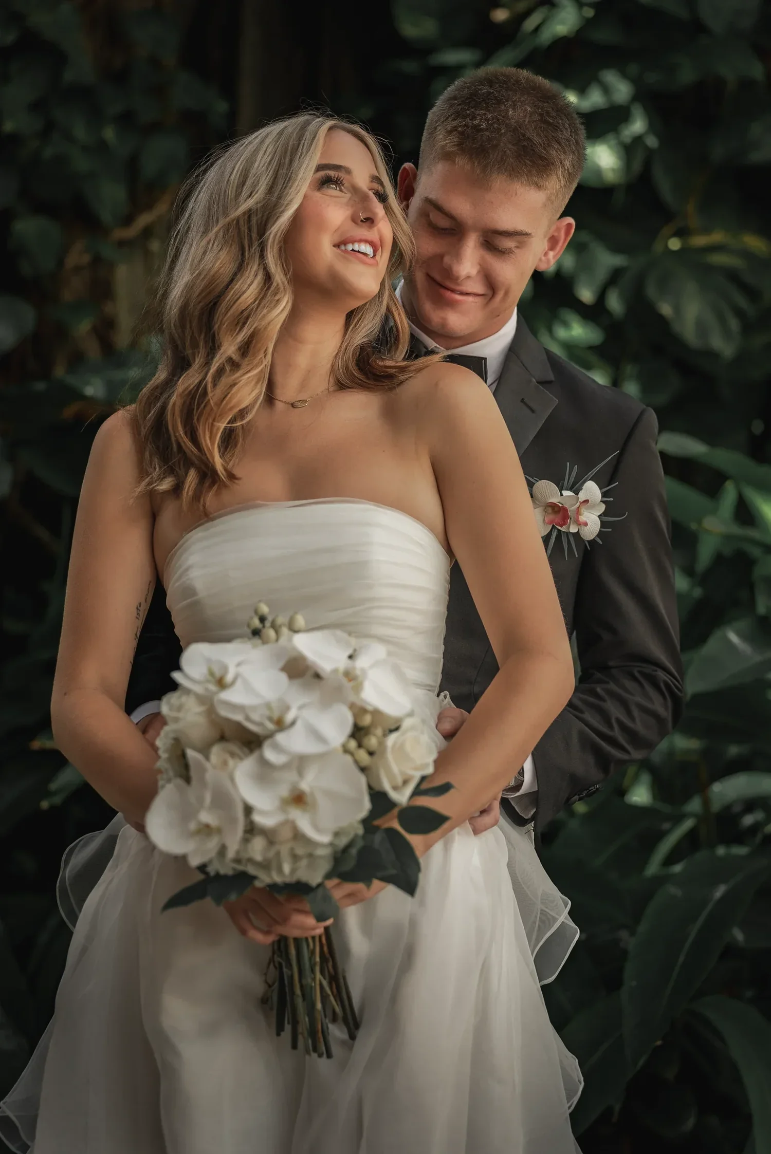 Newlyweds laughing together among tropical leaves at their Hawaii wedding, photographed by BlackTie Brothers