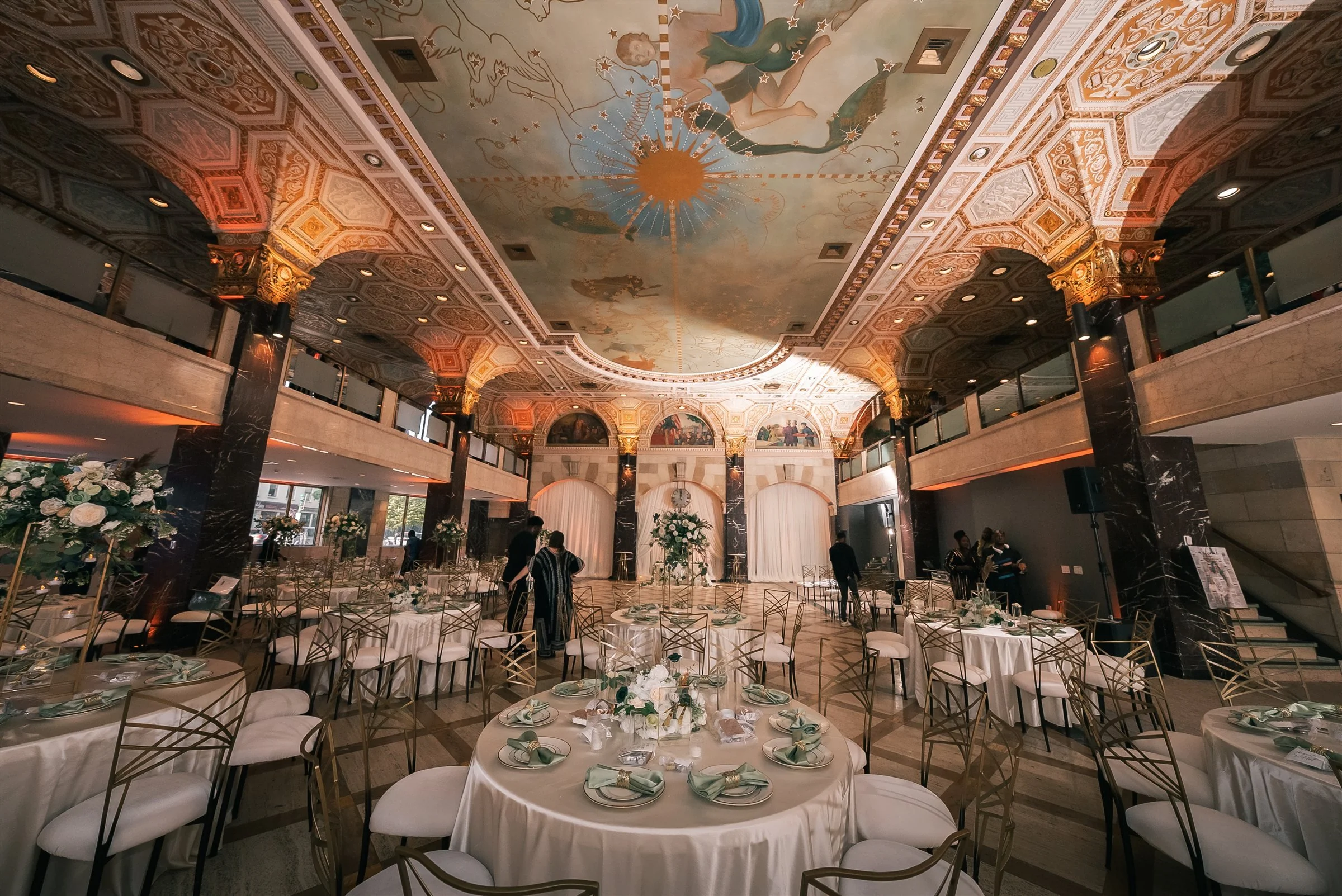 Wide view of Palladian Hall’s painted ceiling, mezzanine and reception tables with white linens and green accents.