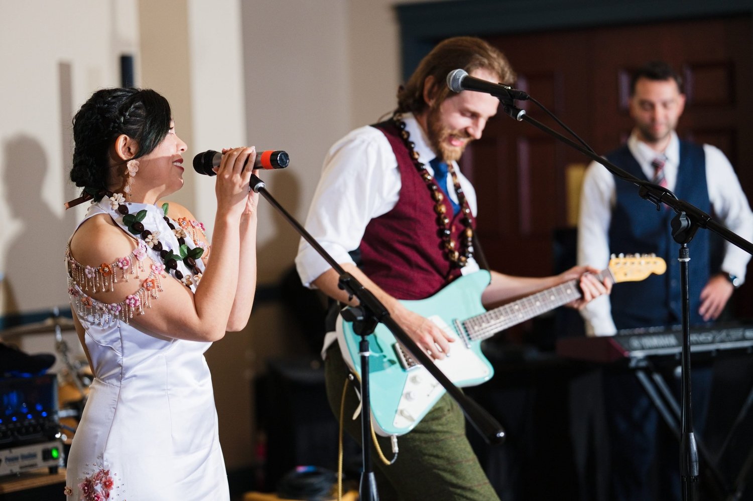 Marseille singing into the microphone while Jason plays a teal electric guitar with the band at their reception