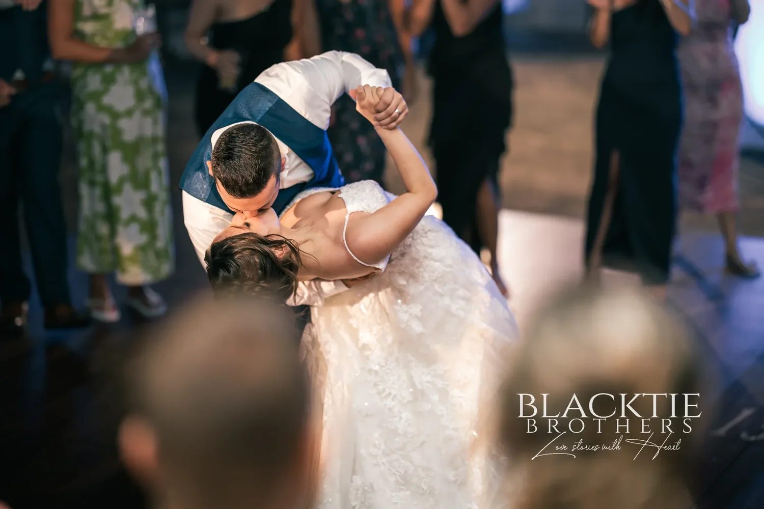 Jake dipping Taylor for a kiss on the dance floor at the end of the night, guests in dresses close around them