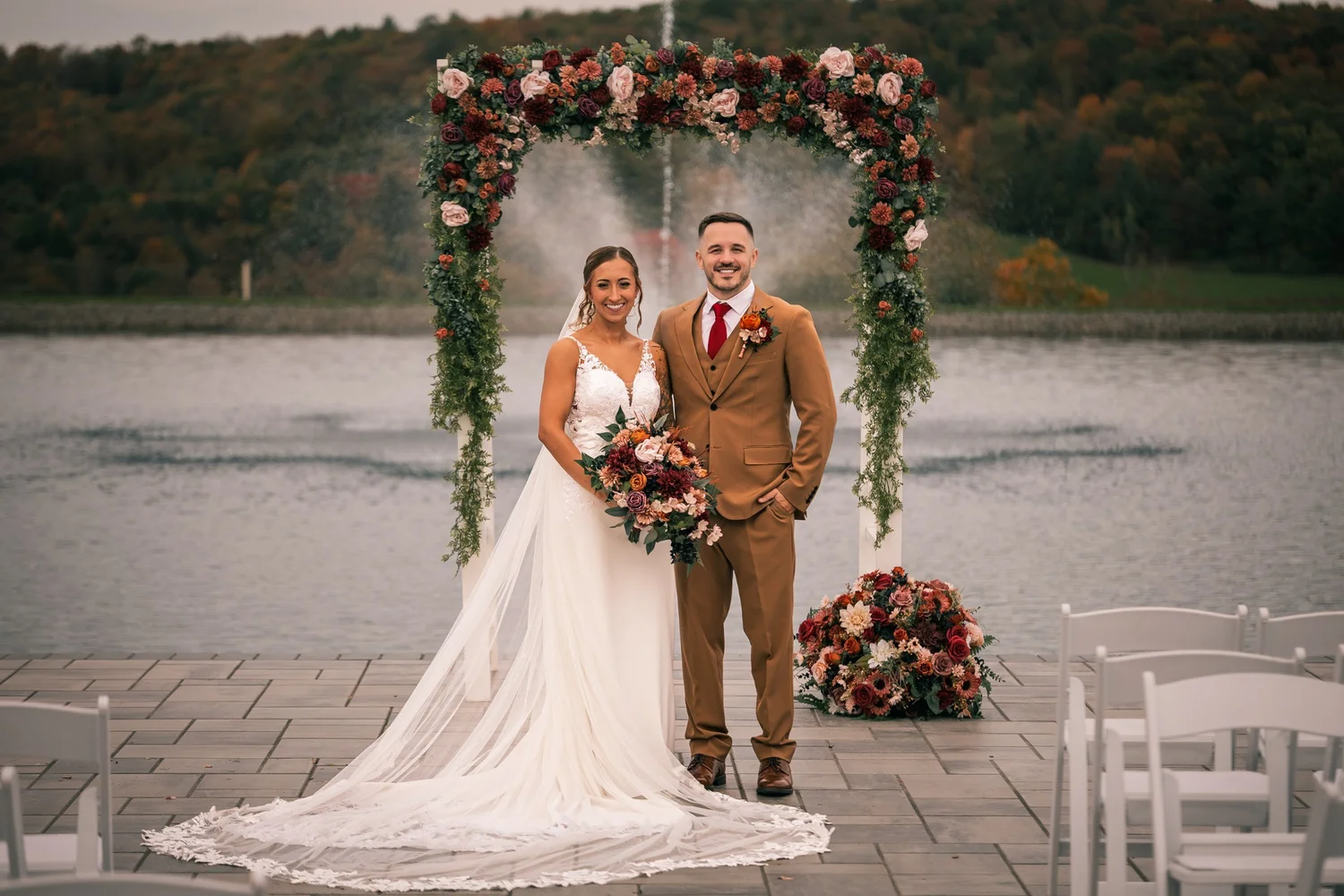 Heather and Vincent under the floral arch after the ceremony, the fountain spraying in the pond behind them