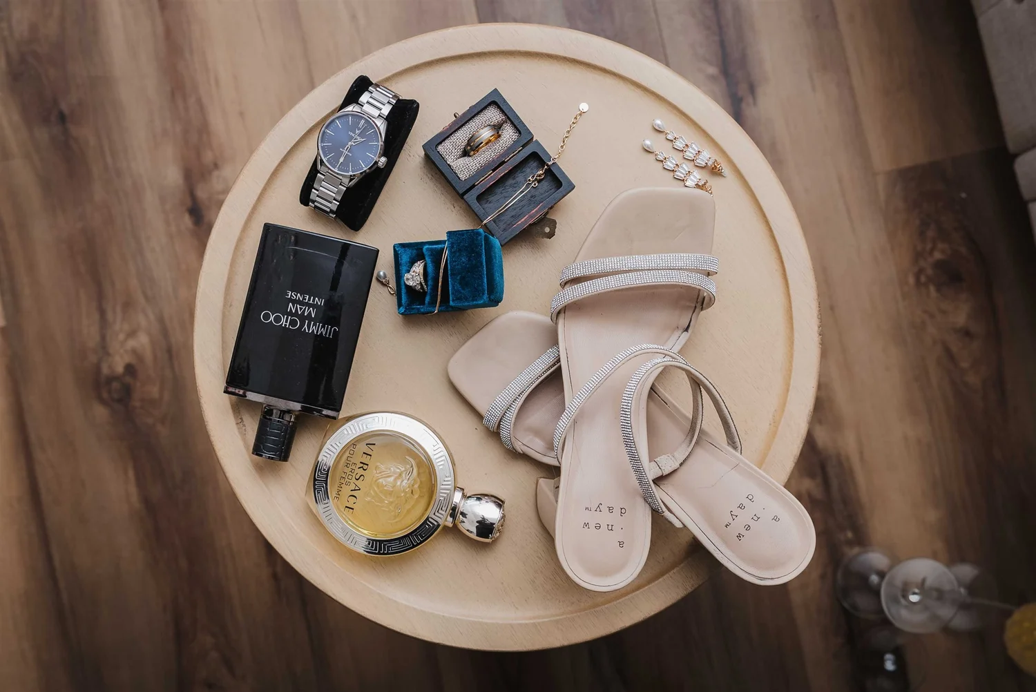 Wedding shoes, ring boxes, a watch and perfume arranged on a round wooden tray.