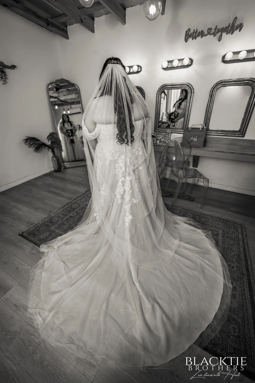 Black-and-white photograph of Alyssa in her wedding gown and long veil, reflected in mirrors in the getting-ready room.