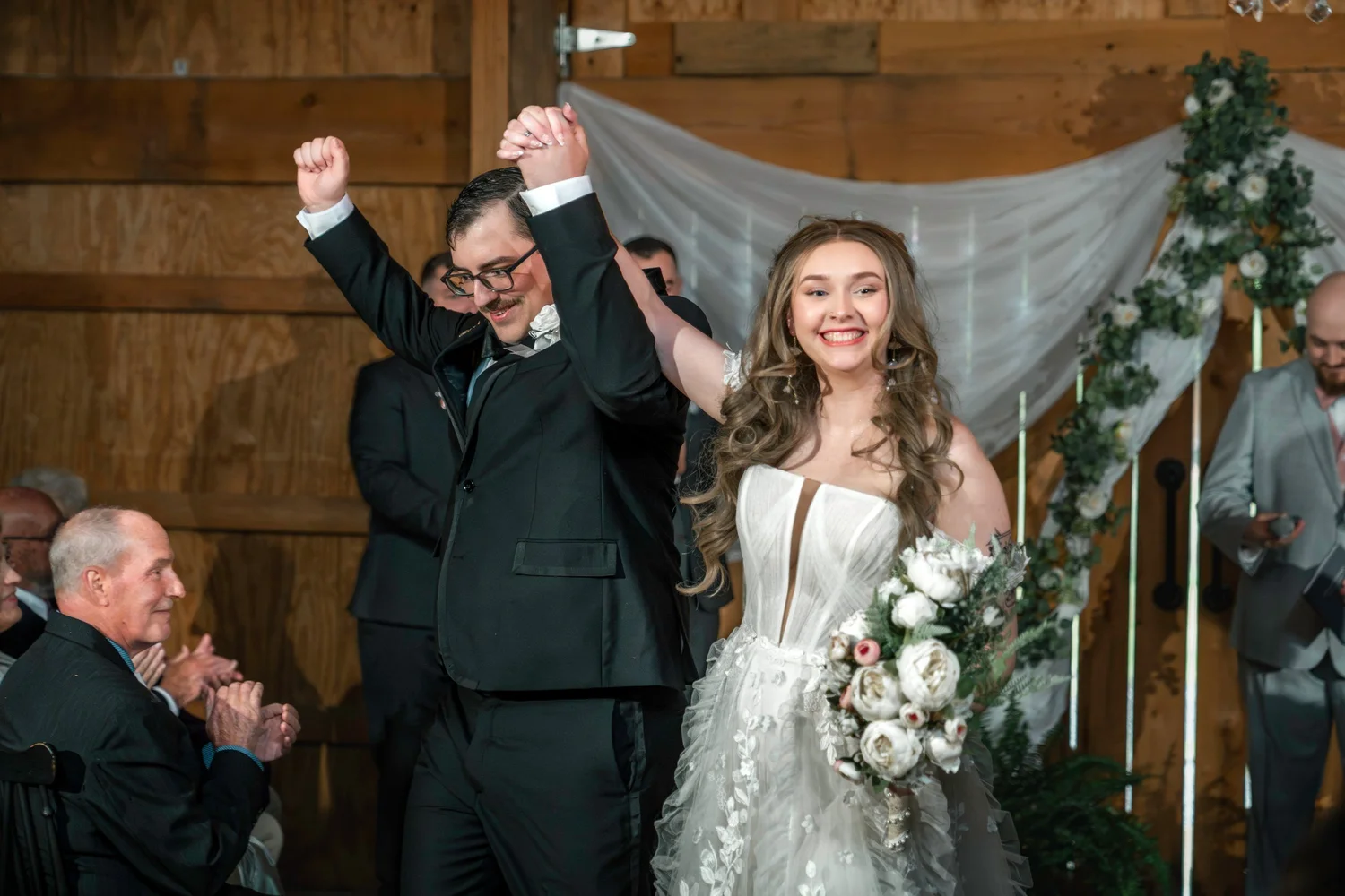 Lindsey and Noah raising their joined hands as they head back up the aisle, guests clapping