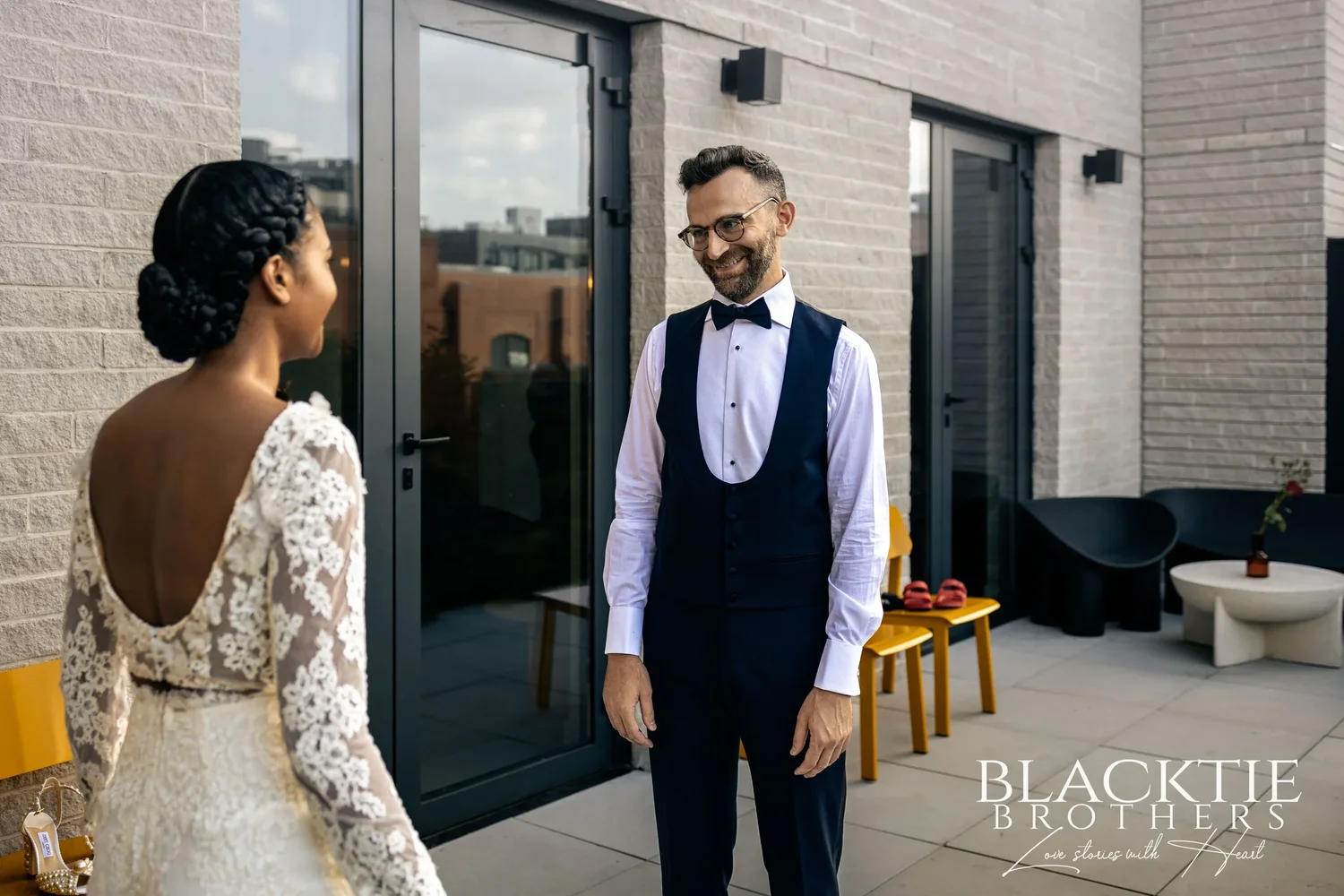 The first look on the rooftop terrace: Ciara seen from behind in her open-back lace outfit, Drew in a vest and bow tie smiling as he sees her