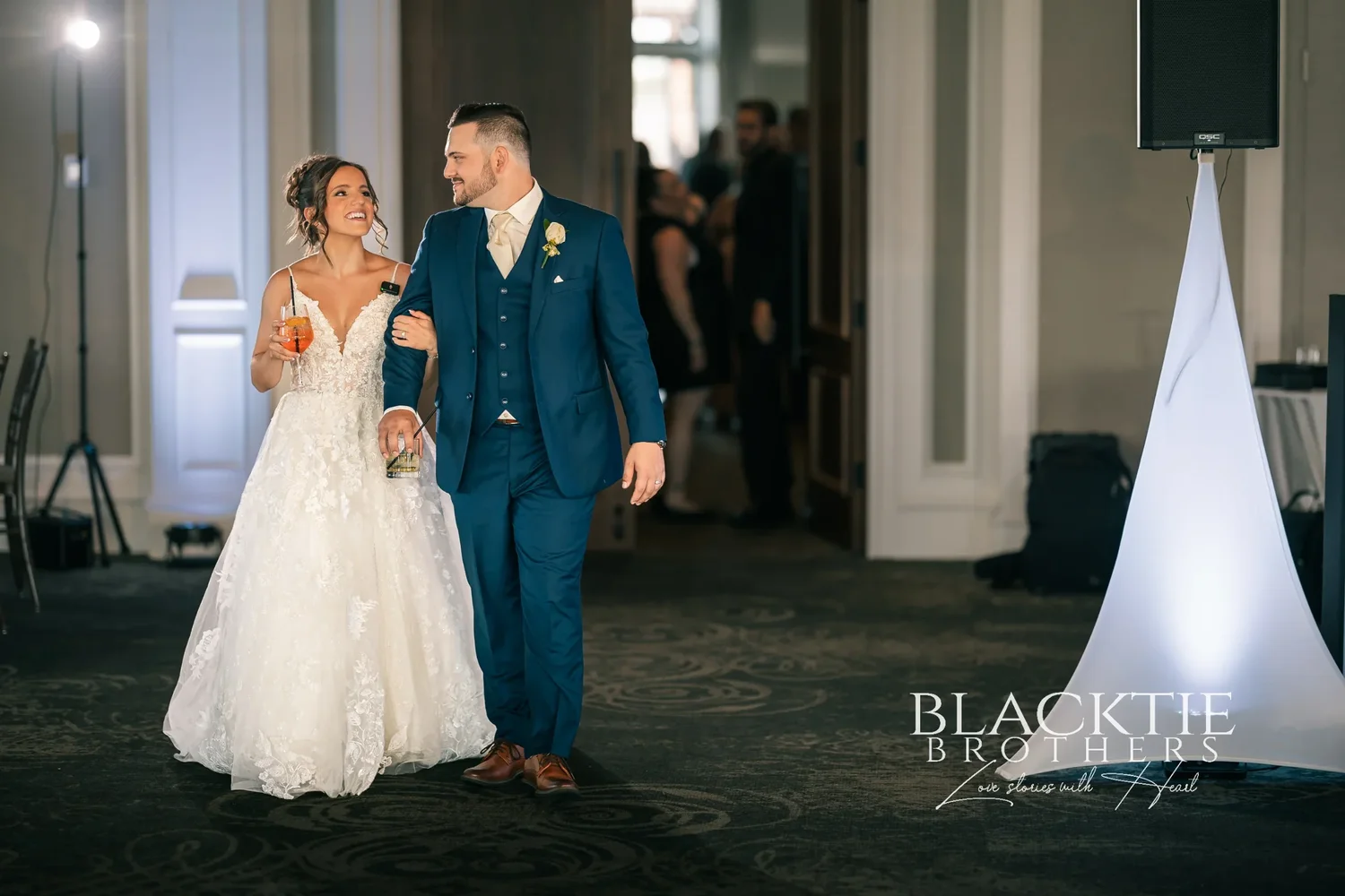 Taylor and Jake entering the ballroom for the first time as a married couple, laughing, with blue uplighting and guests behind them