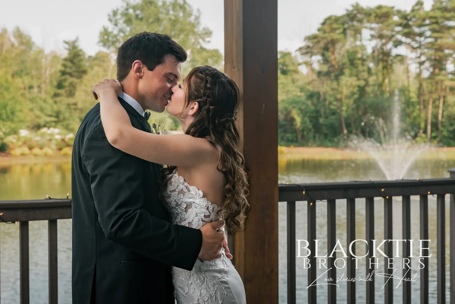 A couple kissing on the deck at Allyn Lodge with the pond and its fountain behind them.