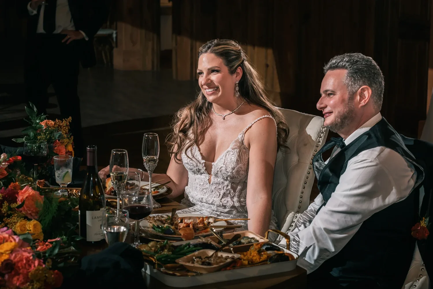 Charissa and Andrew laughing at their sweetheart table during the toasts, autumn flowers and dinner plates in front of them