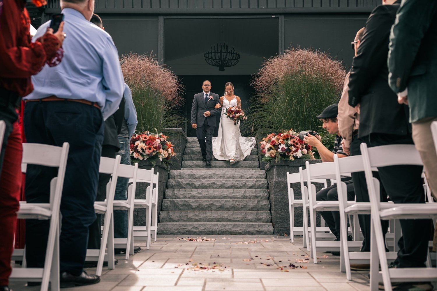 Heather coming down the stone steps toward the aisle as guests turn to watch