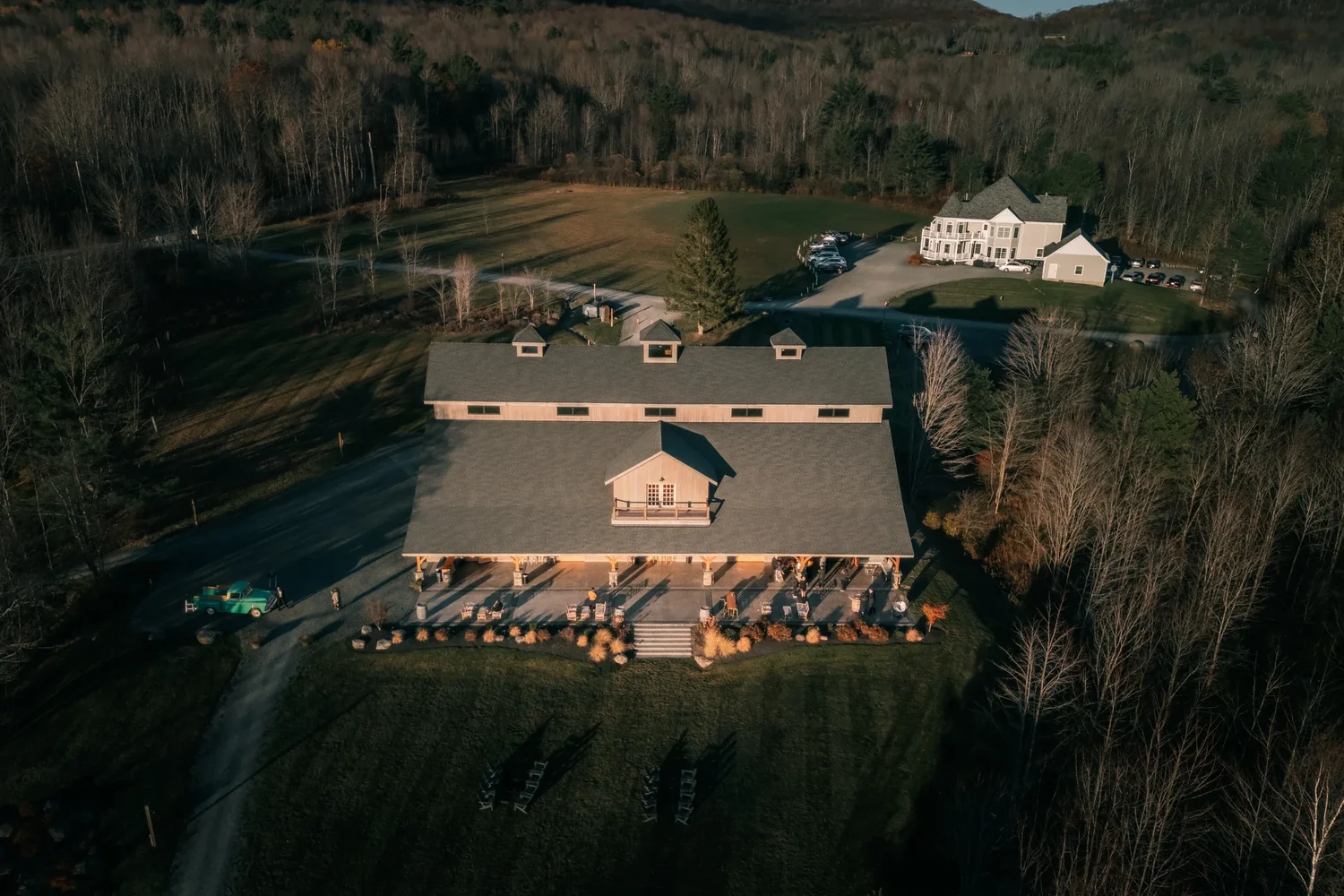 Aerial view of Windham Manor in autumn: the timber Barn with its patio in the foreground, the white Victorian Manor House beyond it and the wooded Catskill Mountains all around