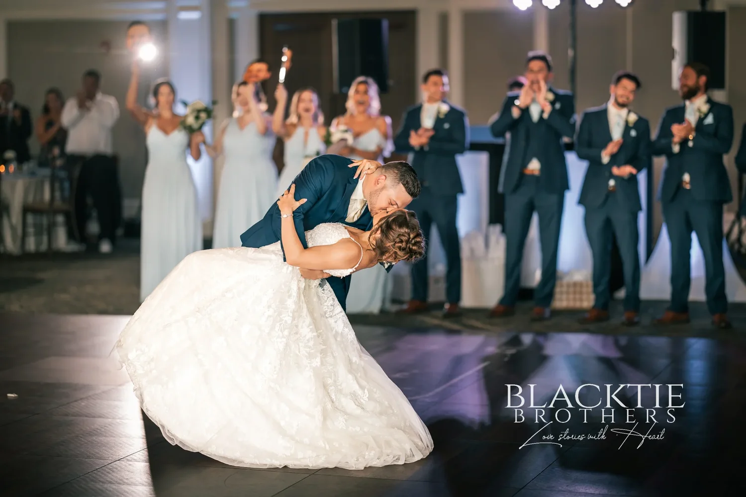 Jake dipping Taylor at the end of their first dance on the dance floor, timber trusses and chandeliers overhead, guests seated at the tables around them