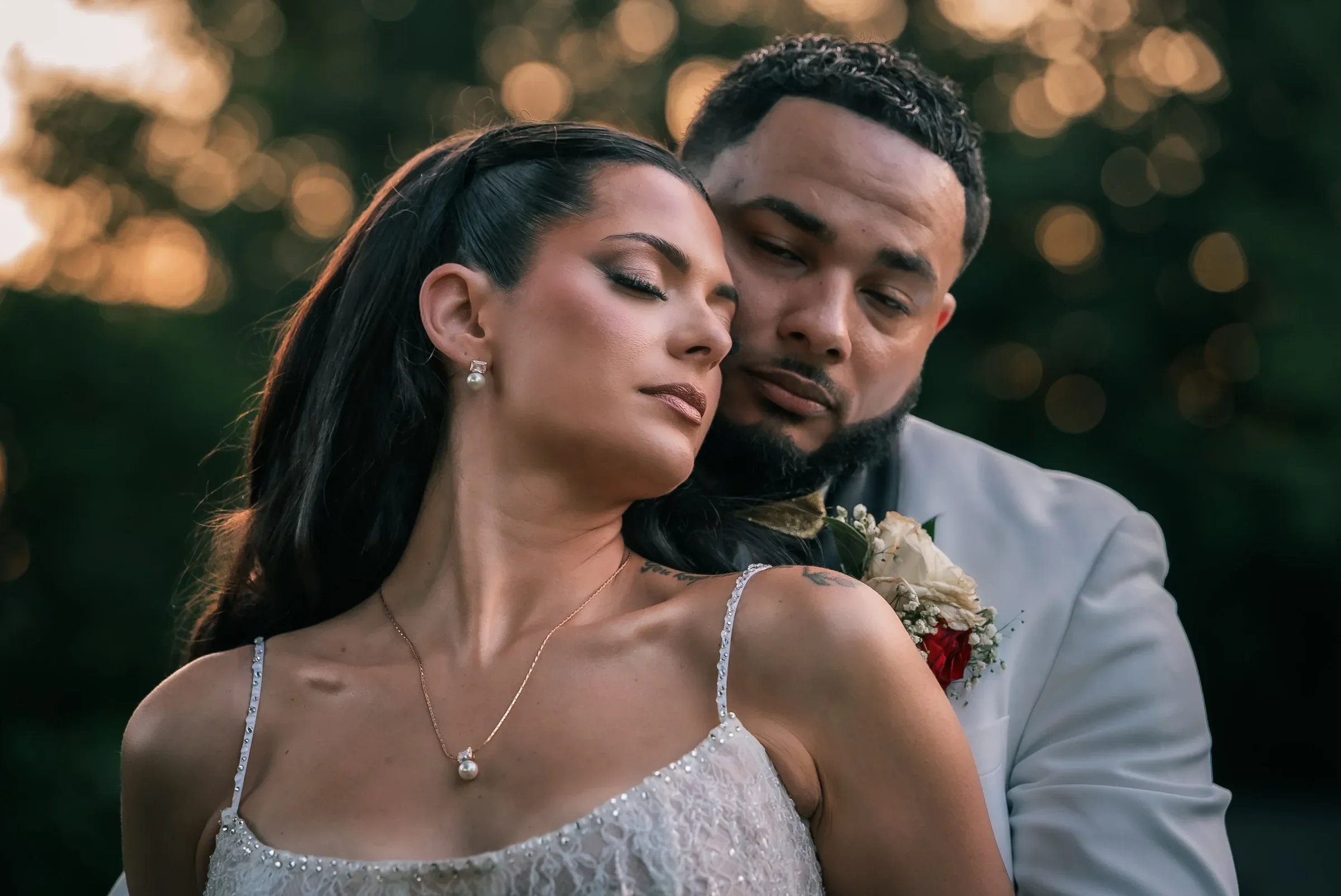 Vanessa with her eyes closed and her cheek against Trevor’s as the low sun glows through the trees behind them