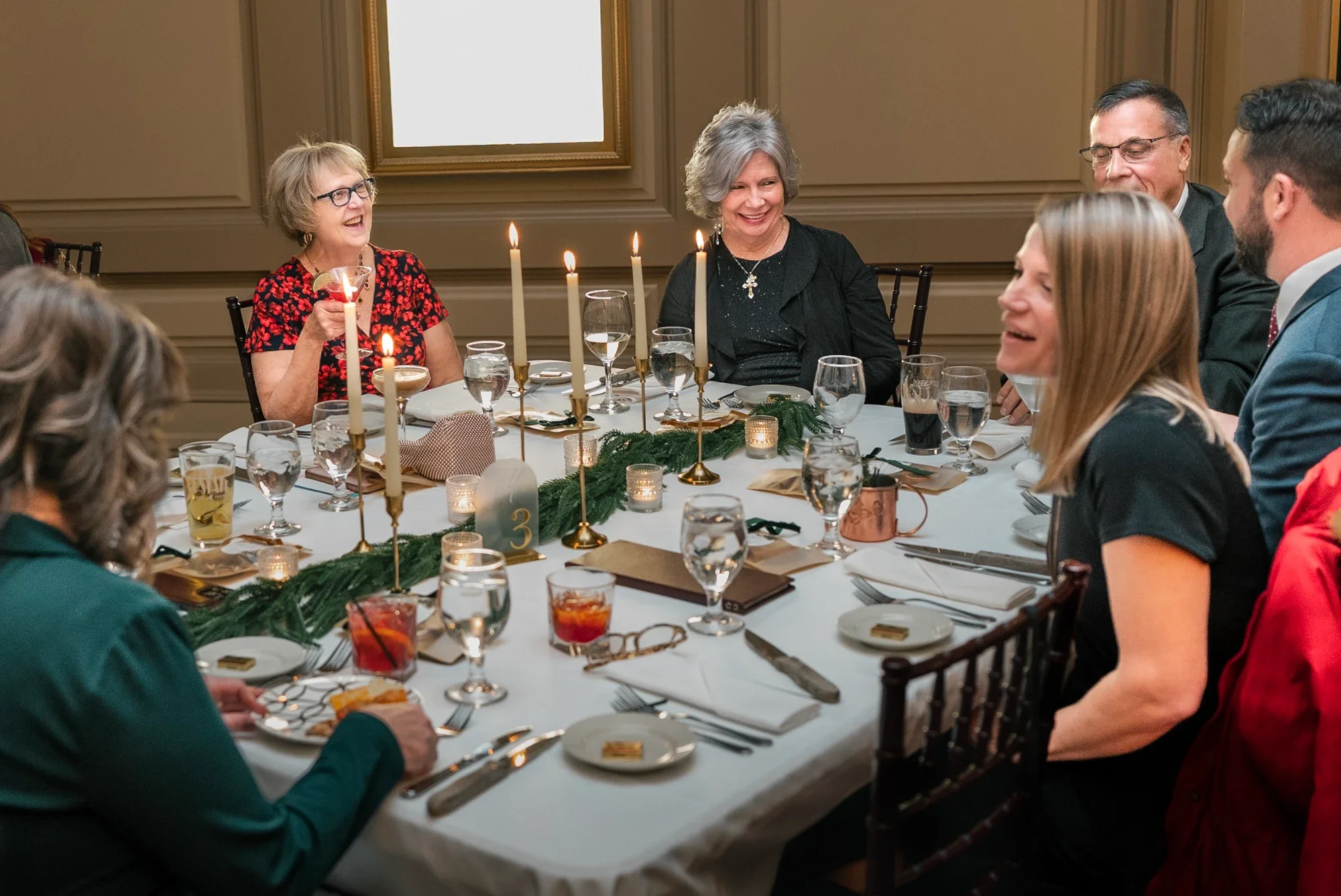 Guests talk across candlelit dinner tables dressed with evergreen runners at Remlik’s.