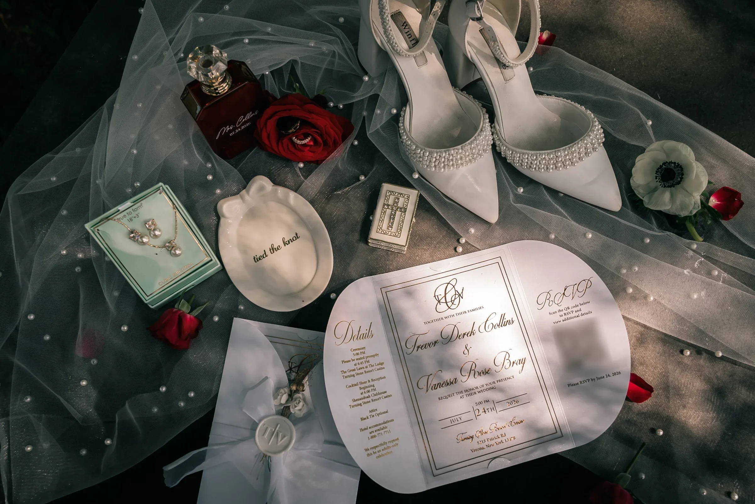 Vanessa and Trevor’s gold-foil invitation, pearl-trimmed heels, pearl jewelry and red roses laid out on a pearl-dotted veil