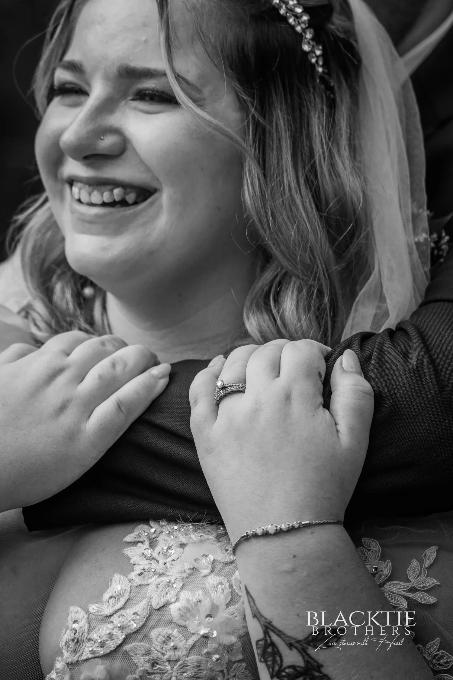 Black and white close portrait of Jennifer laughing with her hands at her chest, her wedding ring and bracelet visible