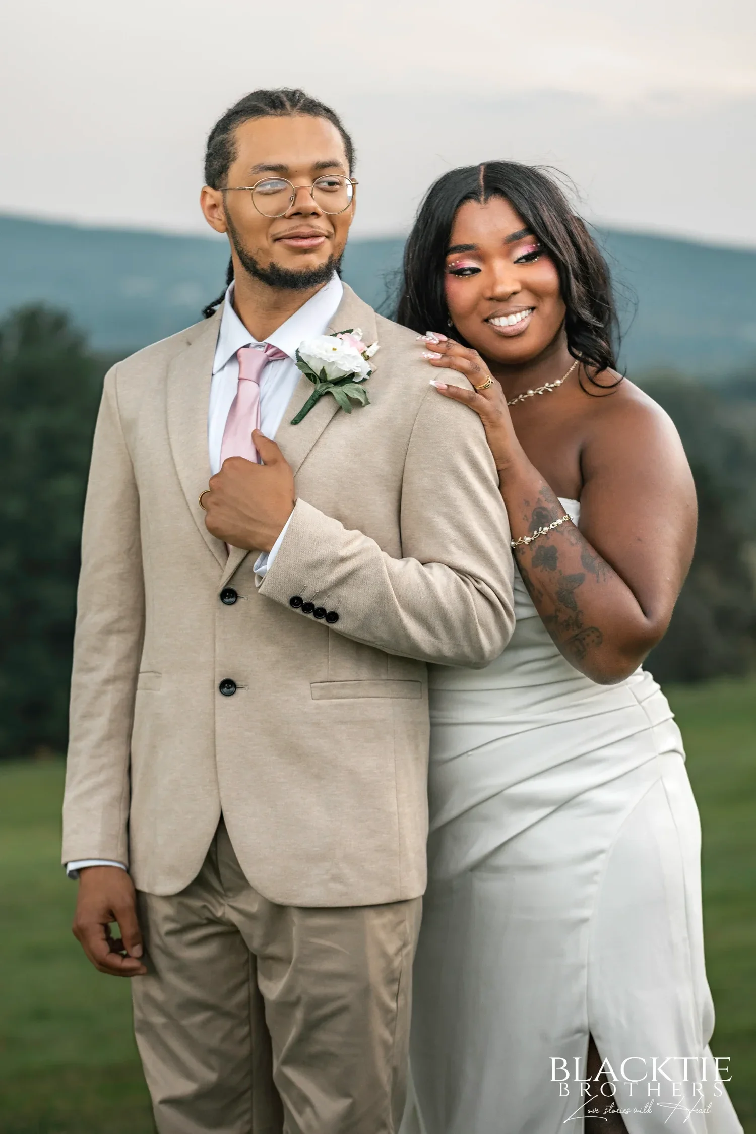 A groom in a tan suit and his bride smiling cheek to cheek on the hill at Traditions at the Glen in soft evening light