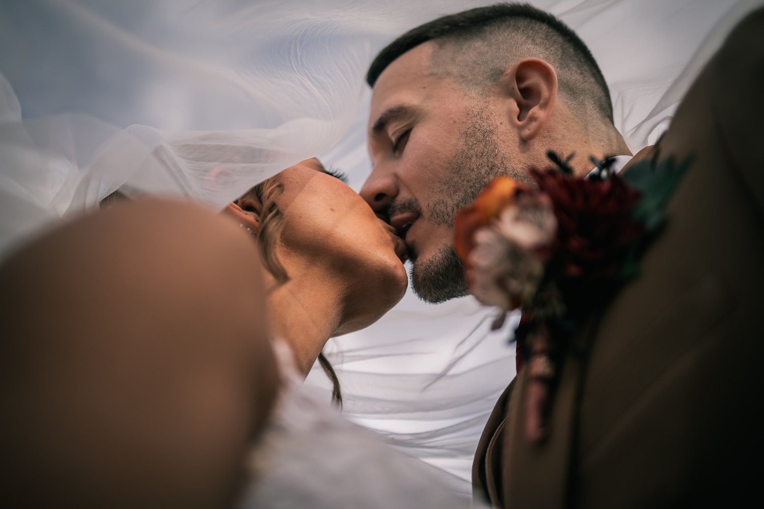 A close kiss under Heather’s veil, Vincent’s boutonniere in the foreground