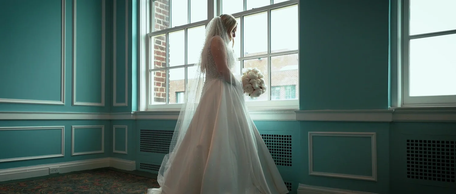 Catie in her wedding dress beside a window in a blue-paneled room at Hotel Syracuse