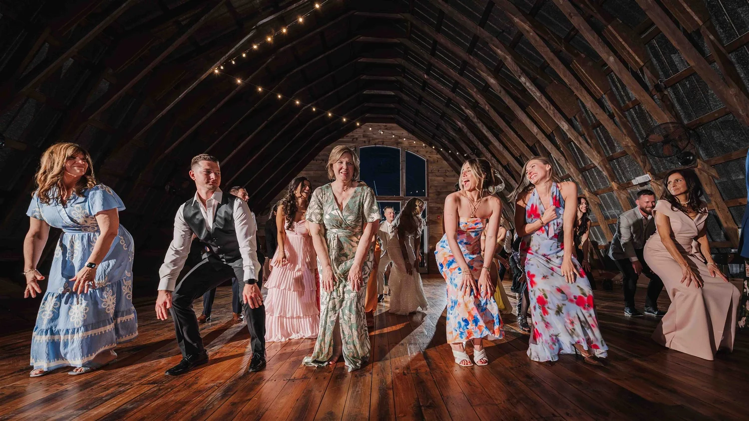 Wedding guests dance in the timber-framed reception room beneath strands of warm lights.