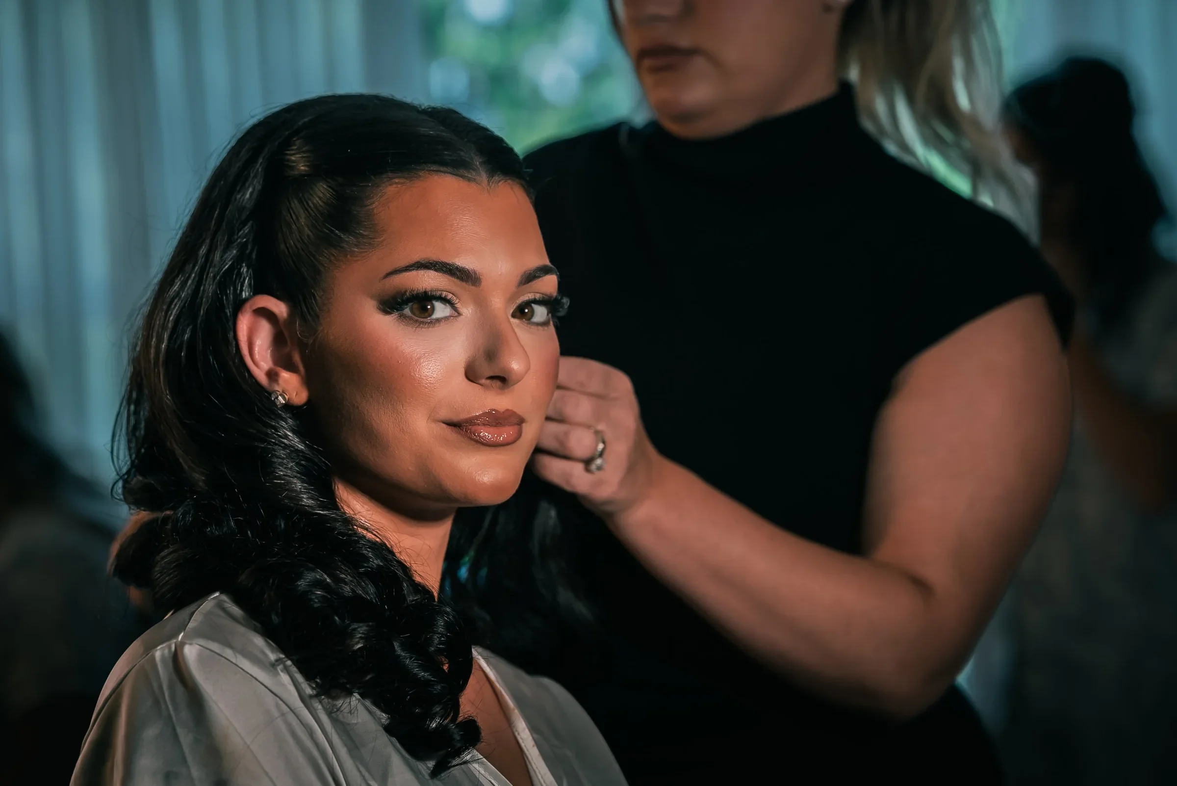 Vanessa in a satin robe looking toward the camera while her stylist sets her curls