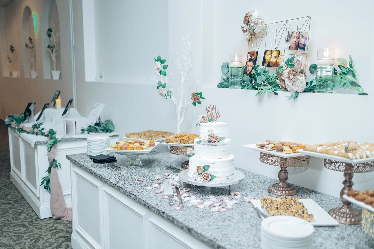 A dessert table with a tiered cake, pastries and framed family photographs along the wall