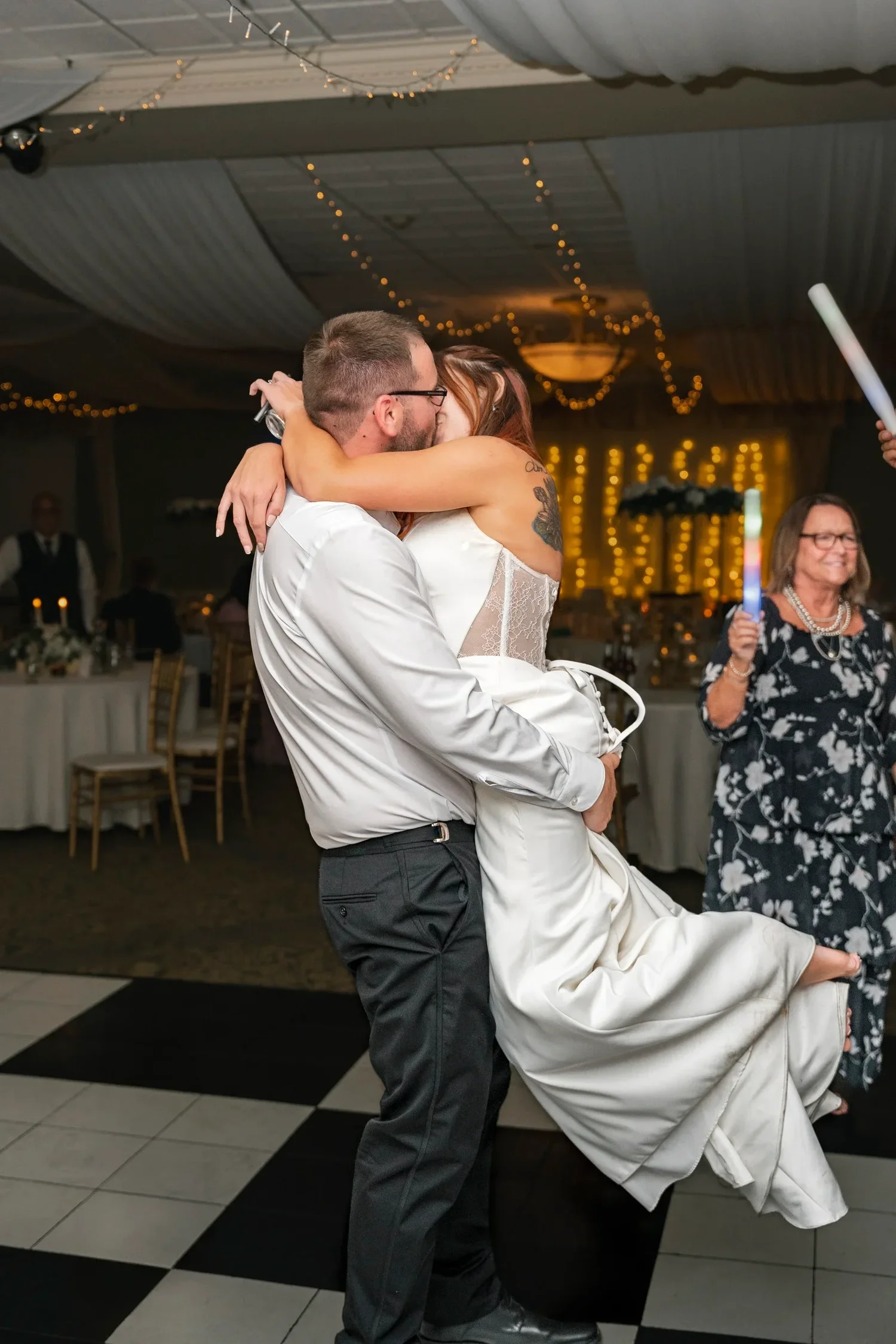 Zach lifting Danielle off the checkered dance floor in a hug at their reception at Traditions at the Glen
