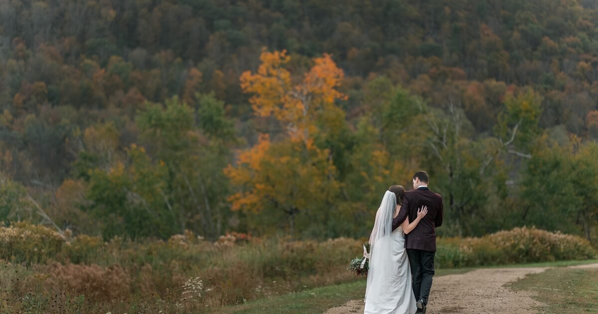 Newlyweds walking together beneath the autumn mountain landscape at Greek Peak