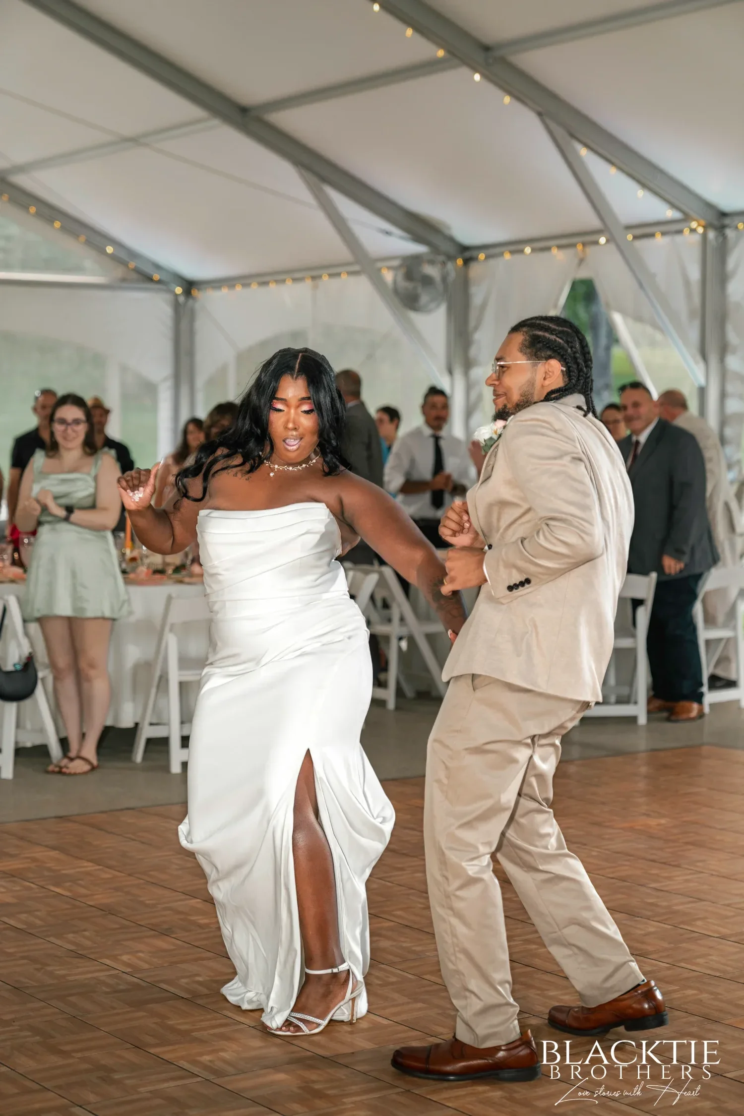 A bride and groom dancing their first dance on the wooden dance floor inside the string-lit reception tent at Traditions at the Glen