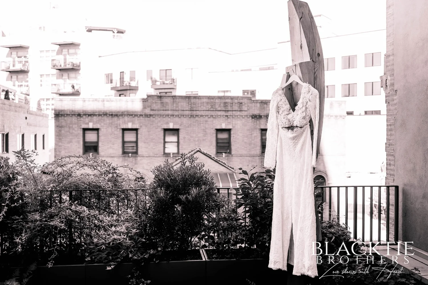 Ciara's long-sleeved lace jumpsuit hanging from a tall wooden stand on a rooftop terrace, planted beds and Brooklyn apartment buildings behind it