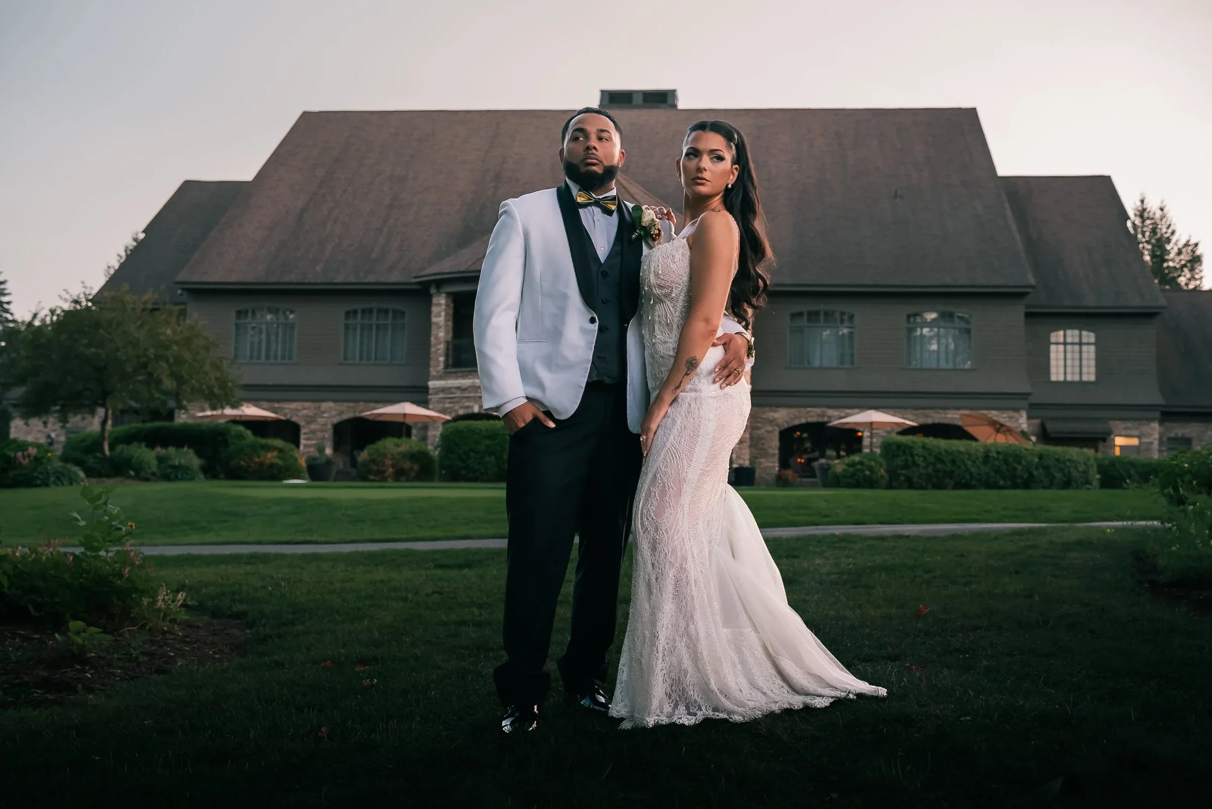 Trevor in a white dinner jacket and Vanessa in a fitted lace gown on the lawn in front of the Shenandoah clubhouse at dusk