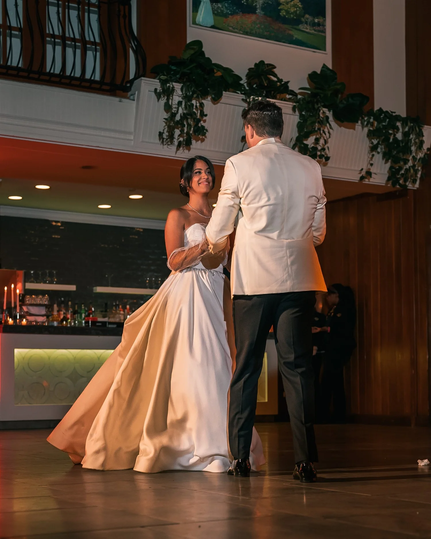 Patricia and Joshua dance together in front of the windows and bar inside The Somerley.