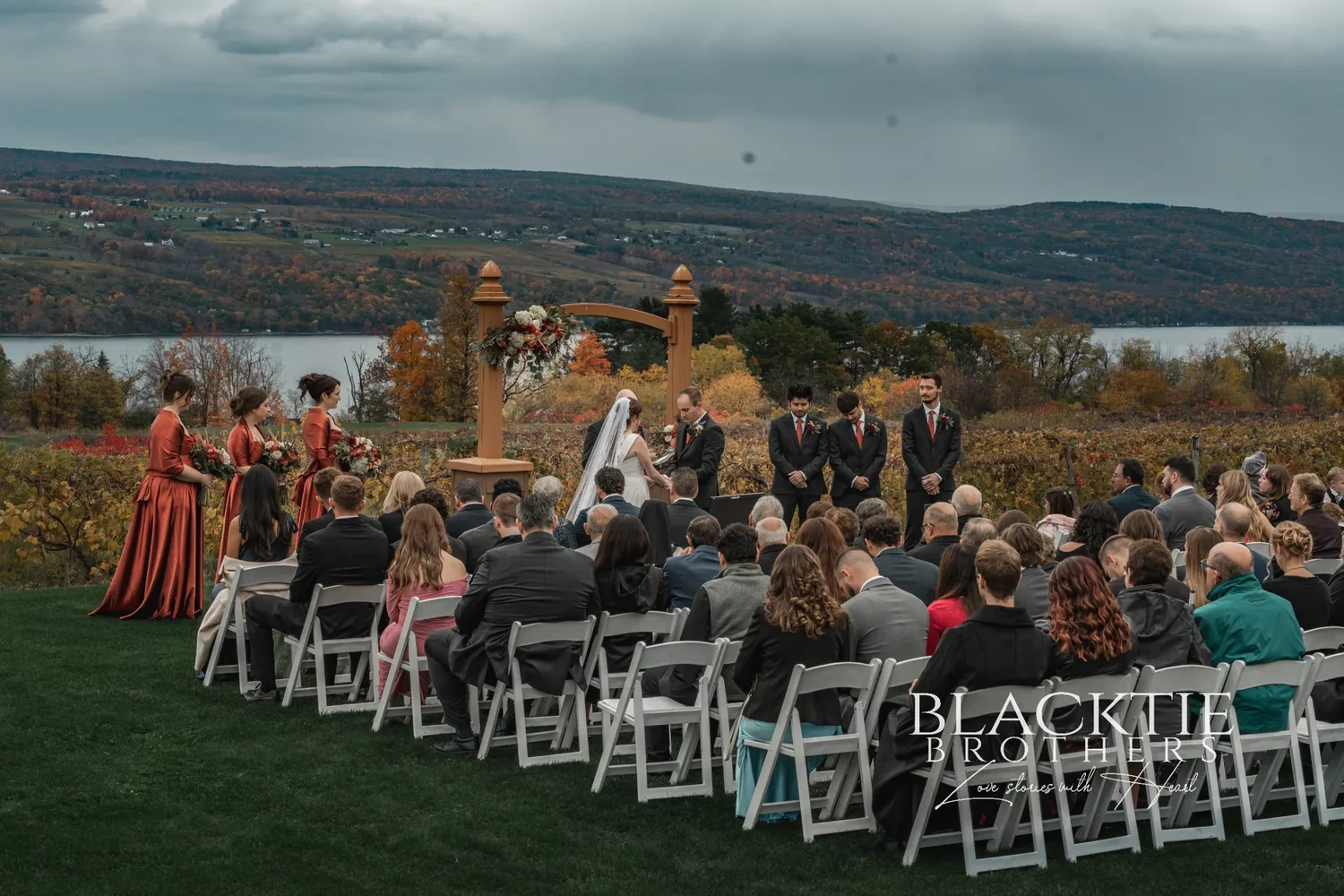 Wedding ceremony at the wooden arbor at Glenora Wine Cellars, guests seated on the lawn, with the vineyard and Seneca Lake behind