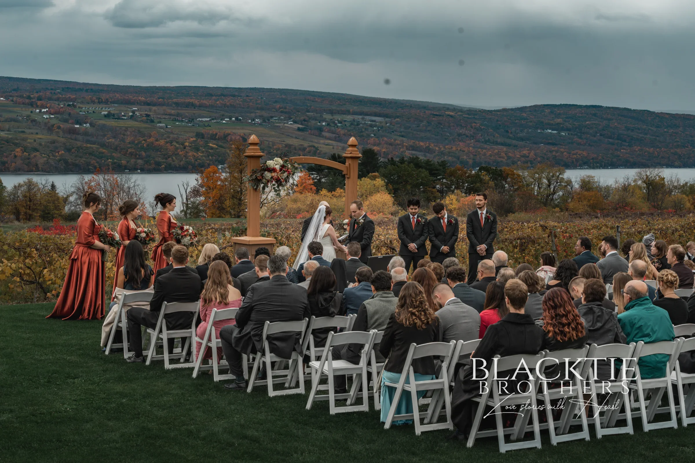 Wedding ceremony at the wooden arbor at Glenora Wine Cellars, guests seated on the lawn, with the vineyard and Seneca Lake behind