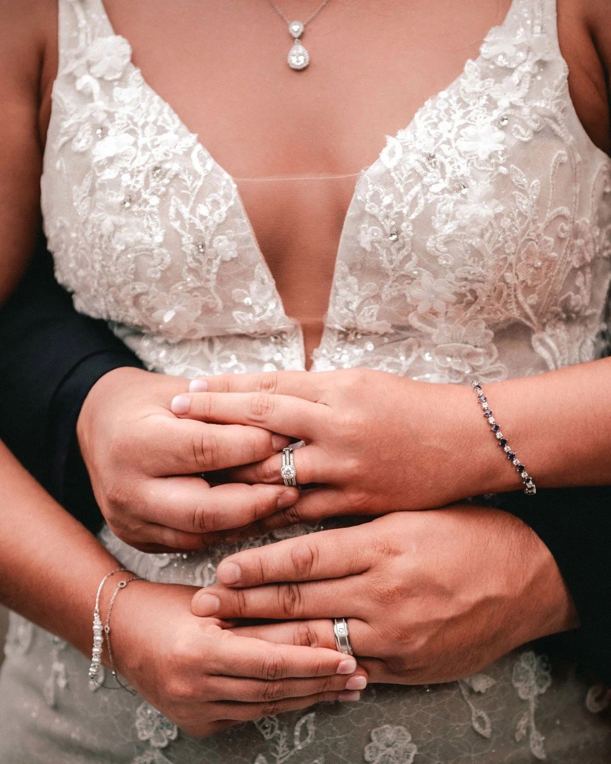 Joelle and Louie’s hands overlap in an embrace, showing their wedding rings against her lace wedding dress.