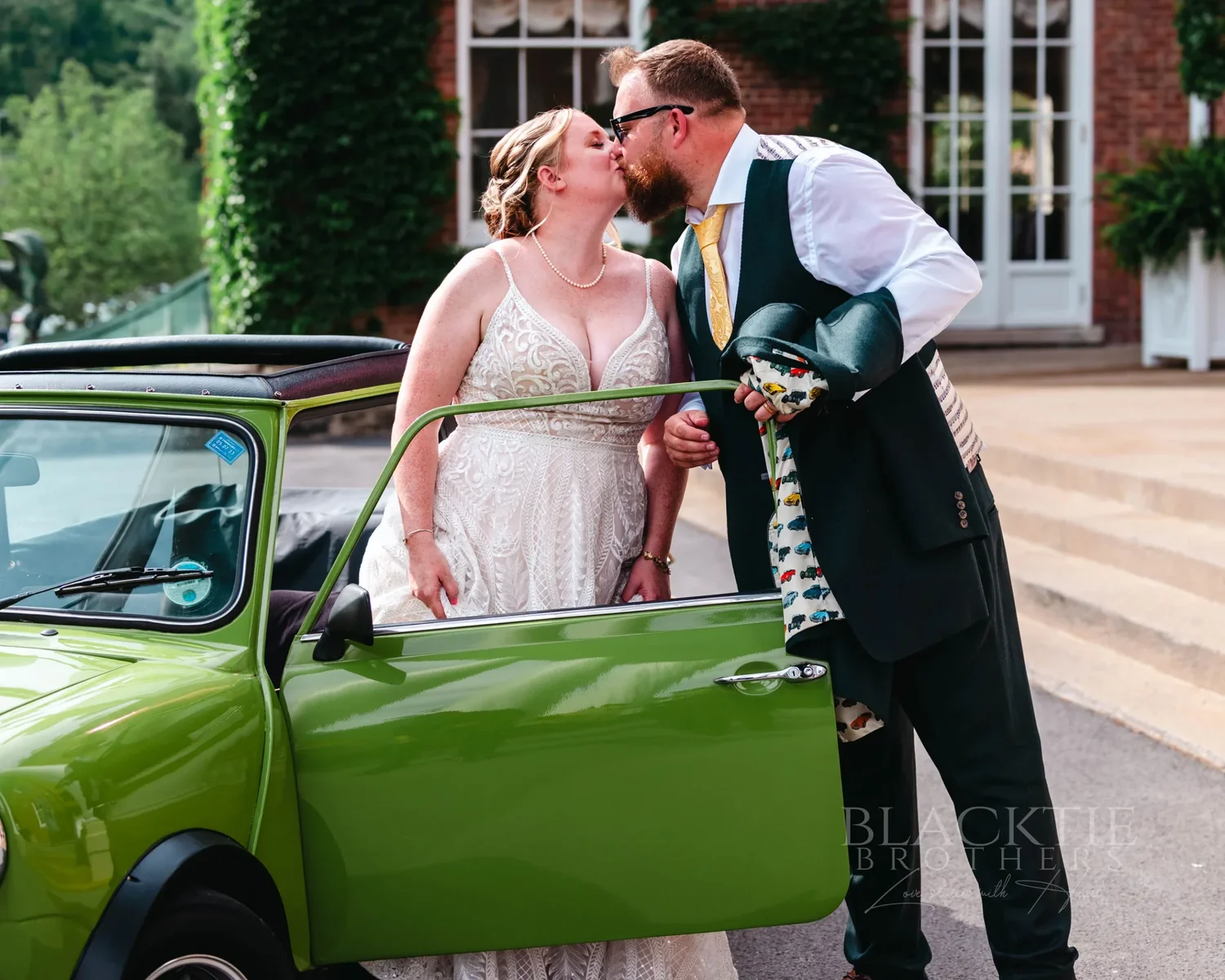 Amanda and Chris kissing beside the open door of the green Mini Cooper at The Otesaga