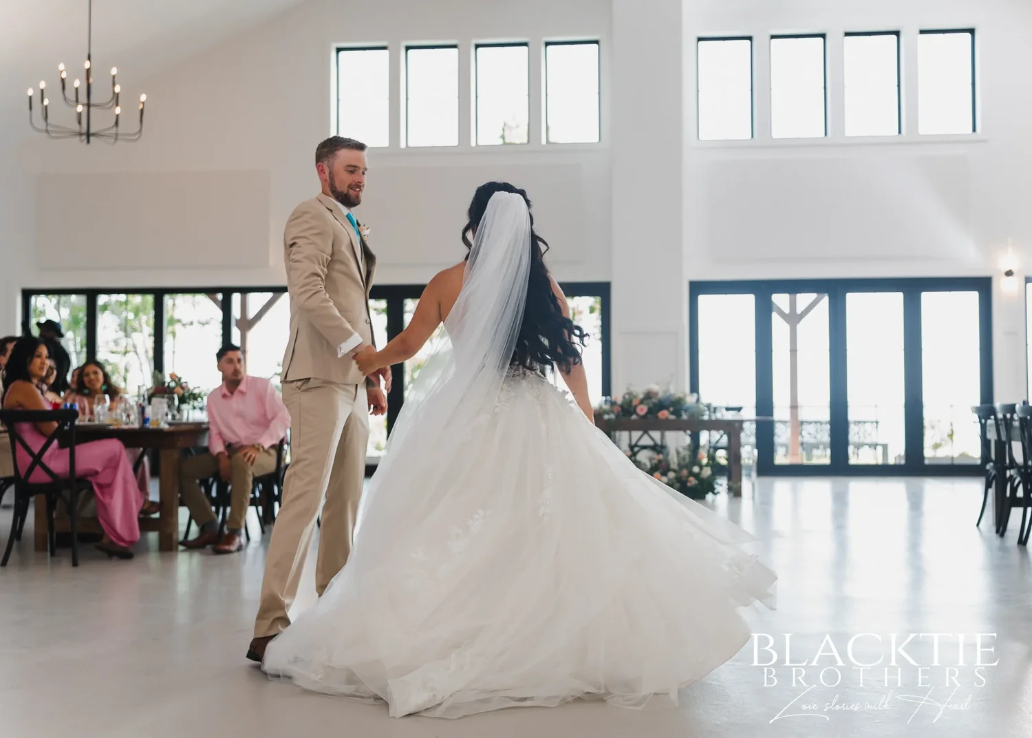 Carolina and Josh's first dance in the bright main hall, her dress swinging out, guests watching from their tables