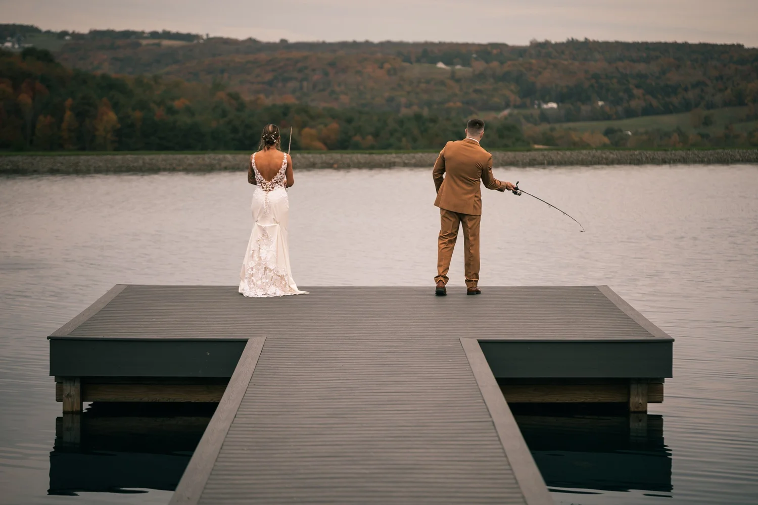 Vincent casting a fishing line off the floating dock while Heather stands behind him in her gown