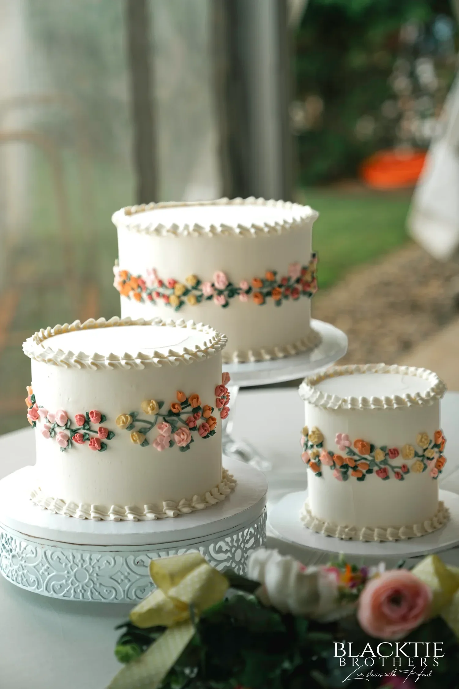 Three small white wedding cakes with piped floral bands on cake stands at a reception at Traditions at the Glen