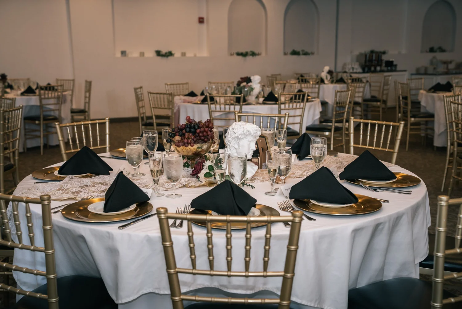 Round reception tables with gold chiavari chairs, black napkins and gold chargers in the ballroom