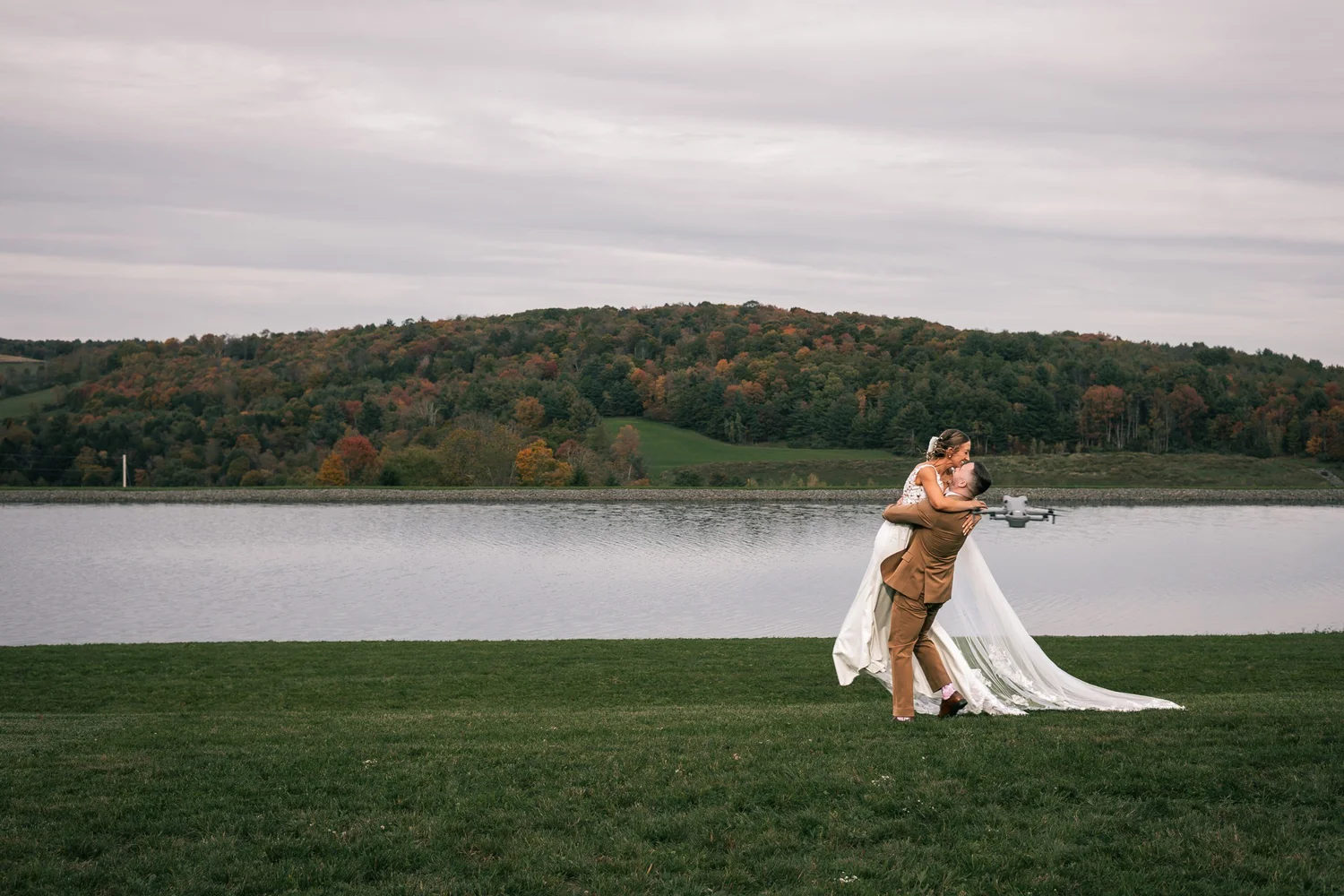 Vincent dipping Heather on the lawn above the pond, with fall-colored hills across the water