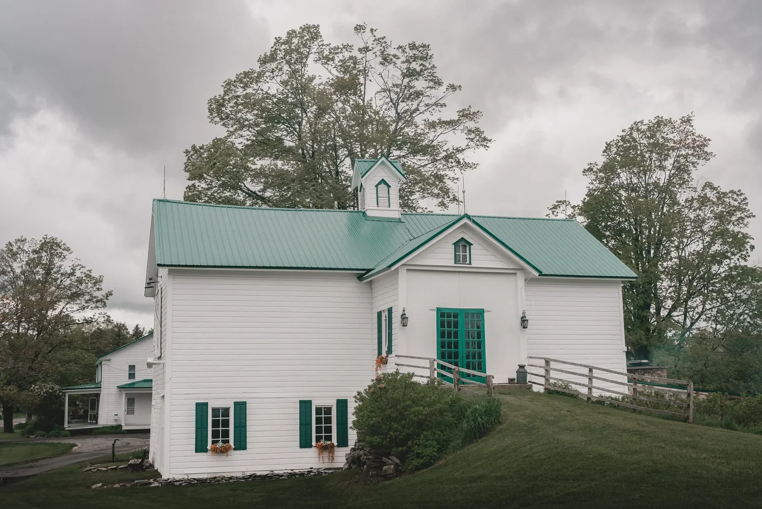 A white barn with green trim, green double doors and a cupola on the lawn at Knotting Hill Farm