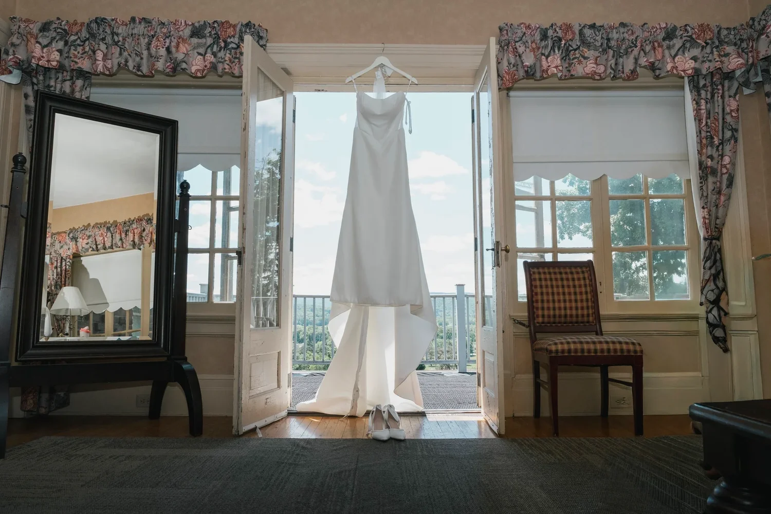 A wedding dress hanging in open French doors in a getting-ready room at Traditions at the Glen, with the hills visible beyond the balcony