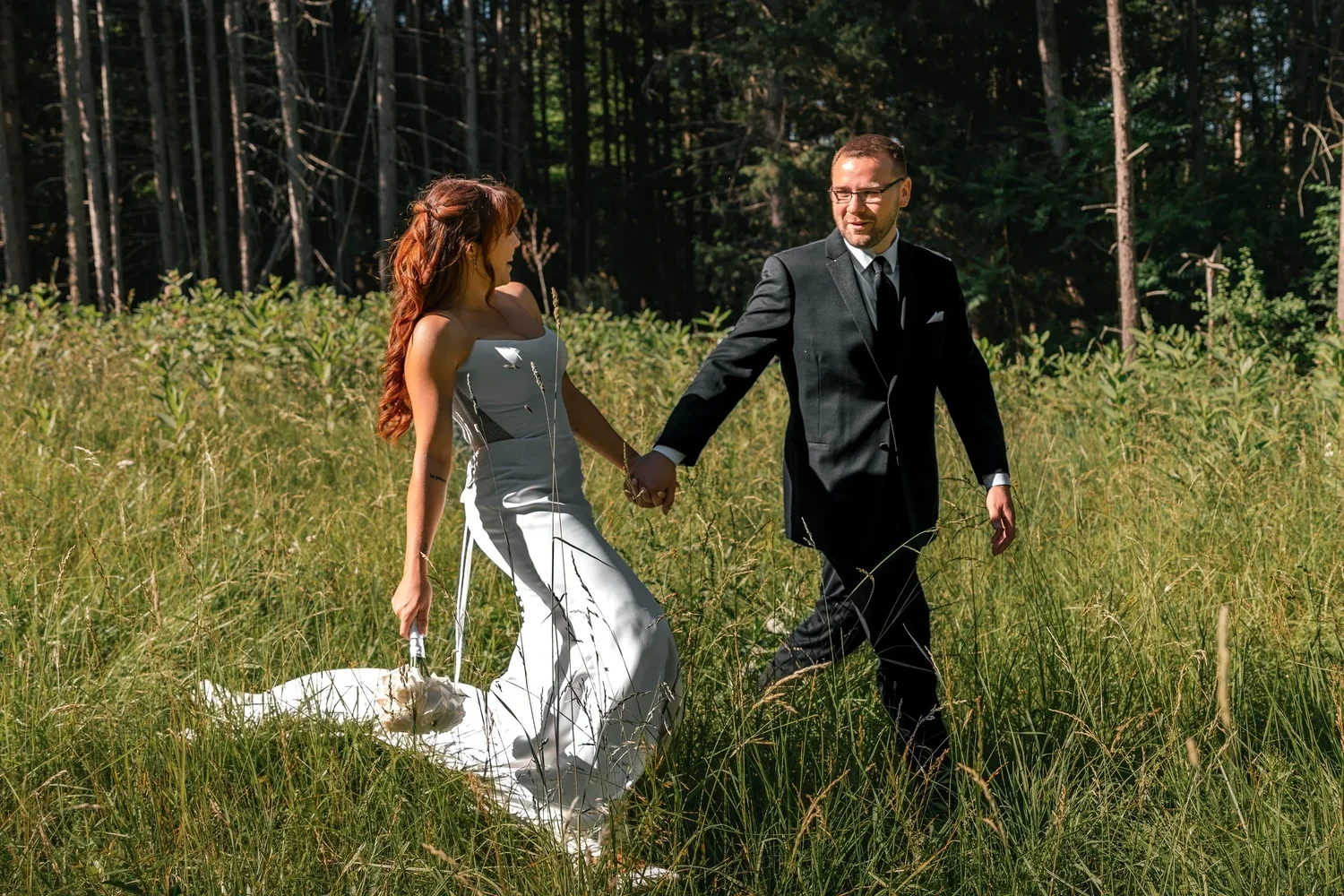 Danielle and Zach walking hand in hand through tall grass at the edge of the grounds at Traditions at the Glen