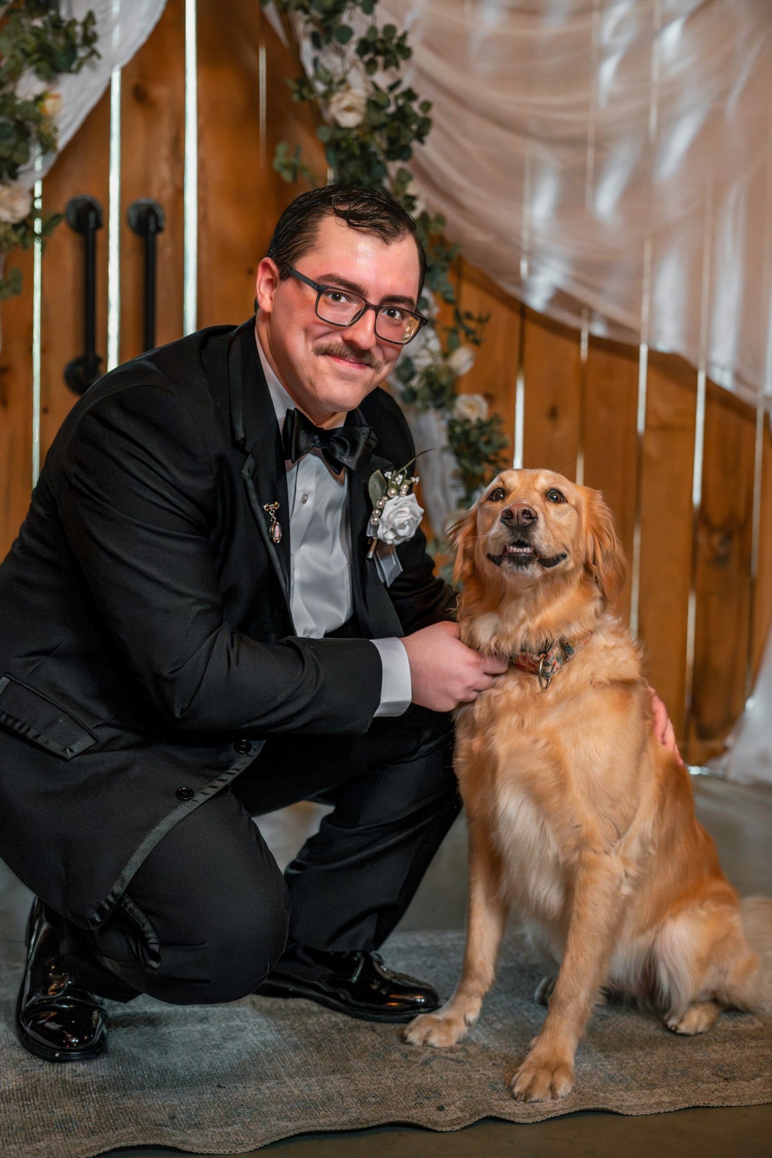 Noah in a black tuxedo crouching beside a golden retriever