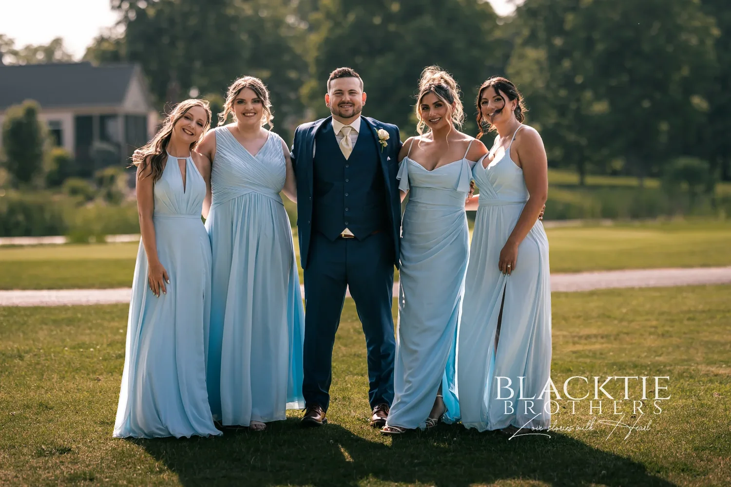 Jake in a navy suit with Taylor's four bridesmaids in pale blue gowns on the course at Timber Banks, houses along the fairway behind them